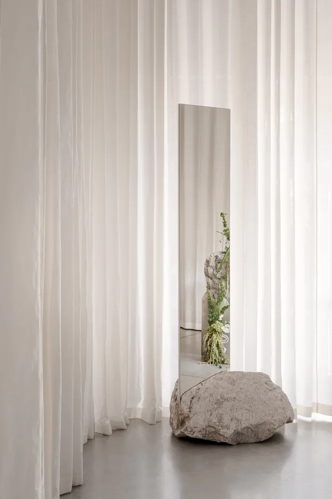 A minimalist interior with neutral materials and a rock-like object in front of sheer curtains.