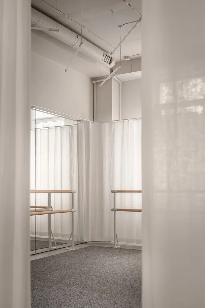 A minimalist dance studio with white curtains and wooden ballet bars.