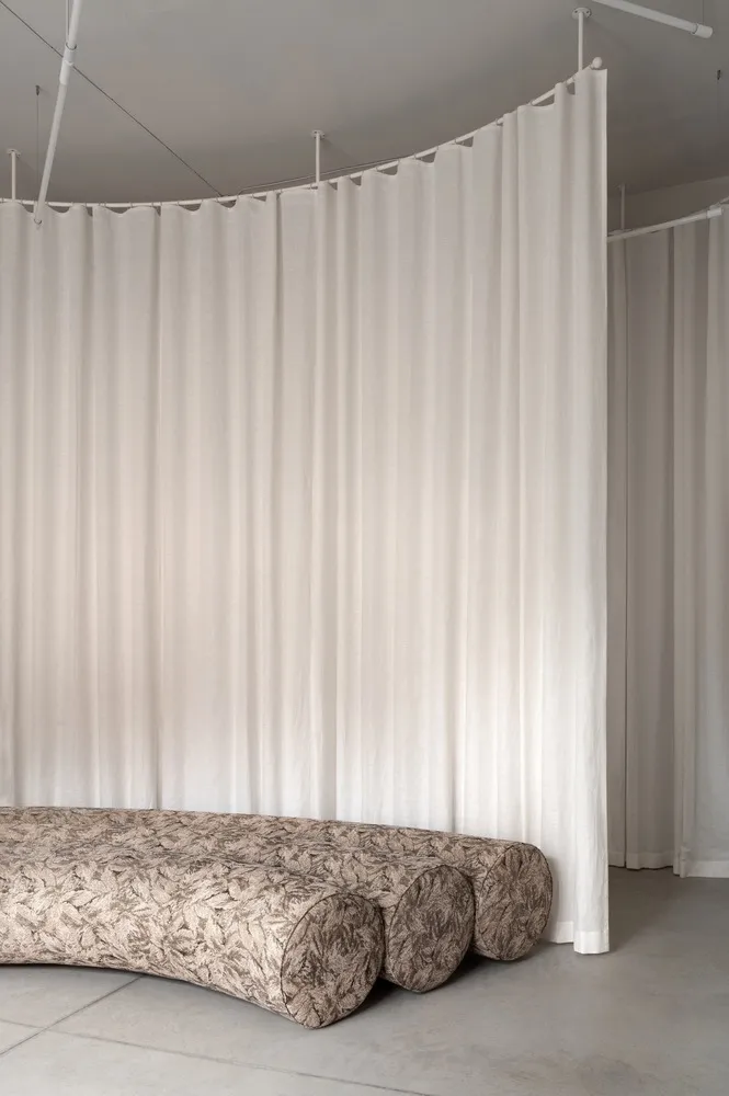 A minimalist sofa upholstered in a printed fabric design, placed against a backdrop of white curtains.