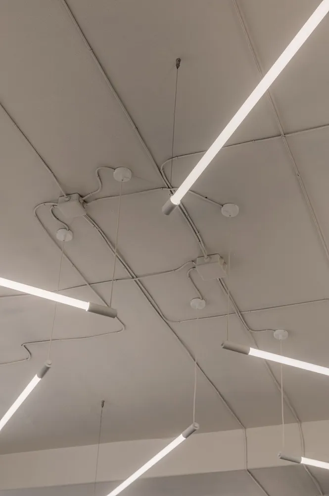 Long modern metallic ceiling lights mounted on white square tiles ceiling