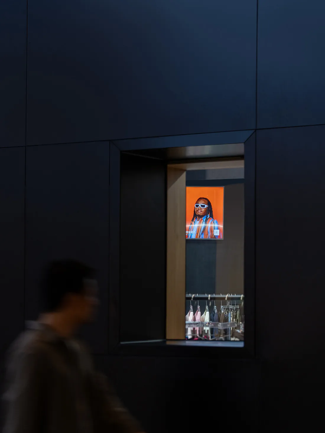 A digital retail display featuring a man with dreadlocks in sunglasses, backlit by an orange background.