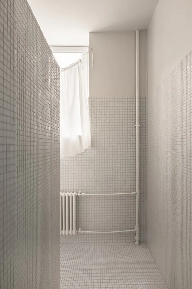 A minimalist bathroom featuring grey tiles and a window with a white curtain.