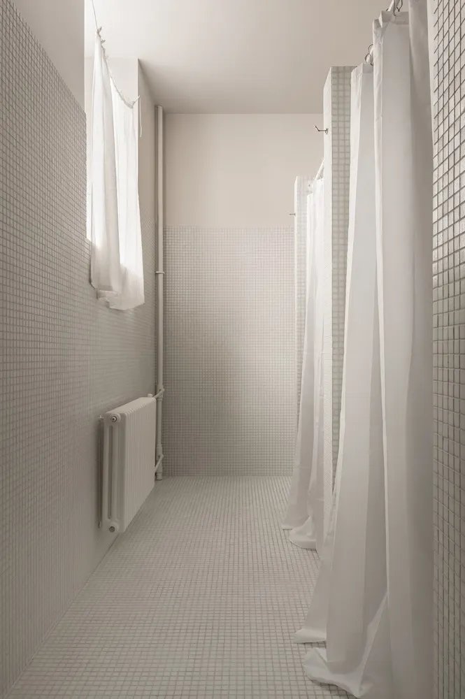 A modern bathroom with white tiled walls and floor, and white curtains.