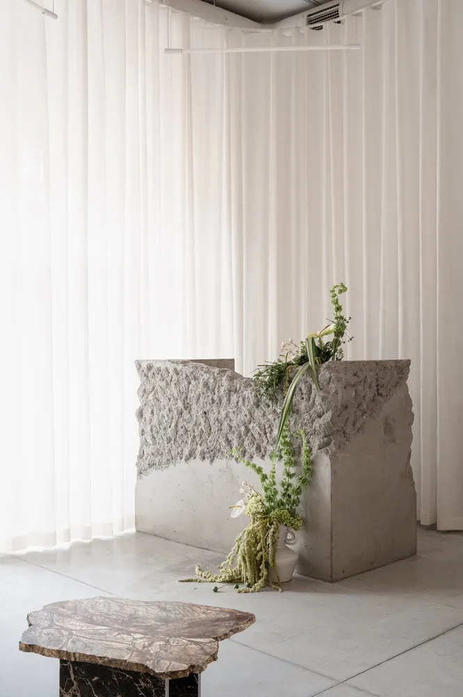 A minimalist, modern room with concrete decor, featuring a vase of greenery and a stone table.