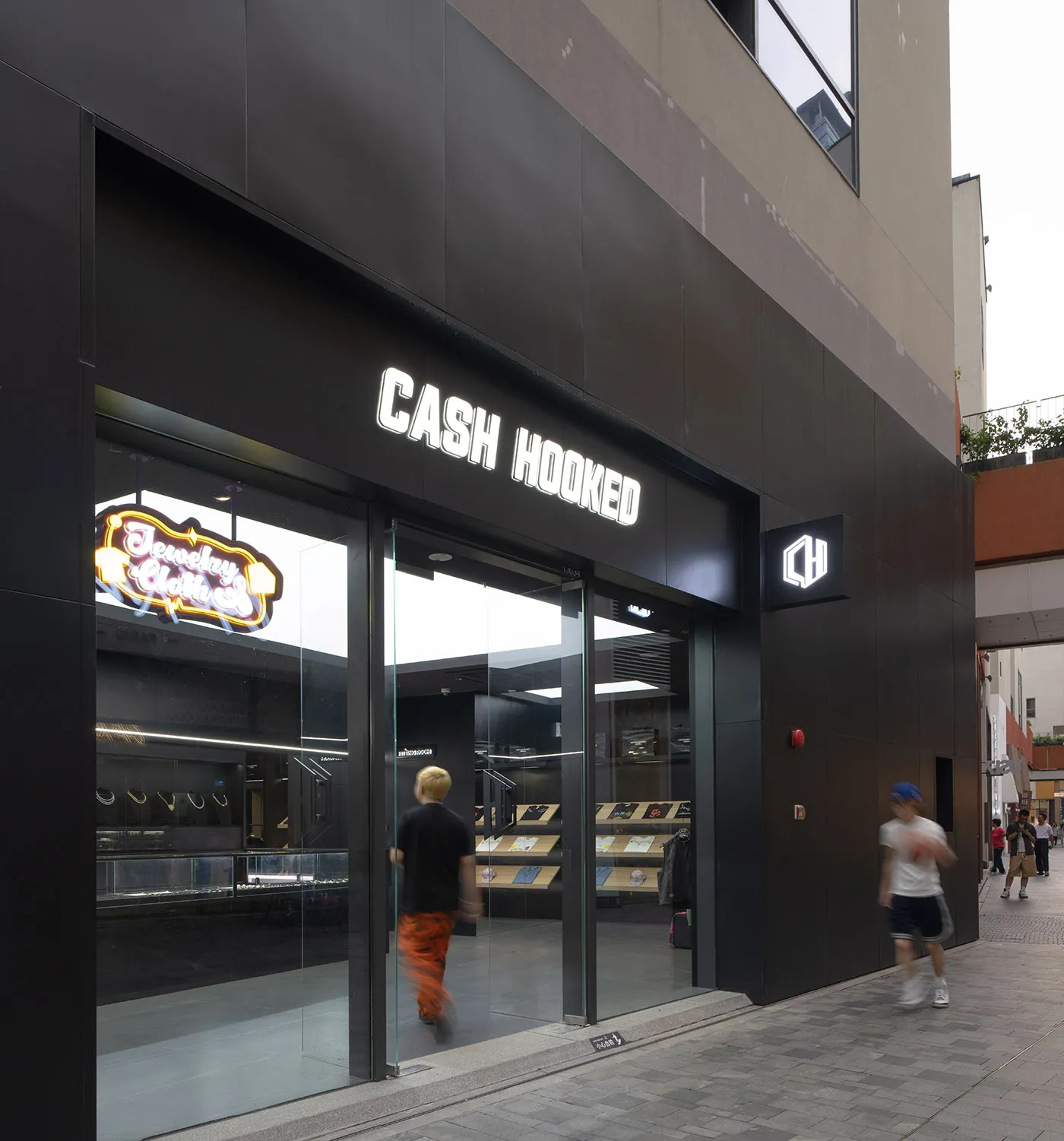 A modern retail storefront with black glass walls and a neon sign displaying 'Cash Hooked'.