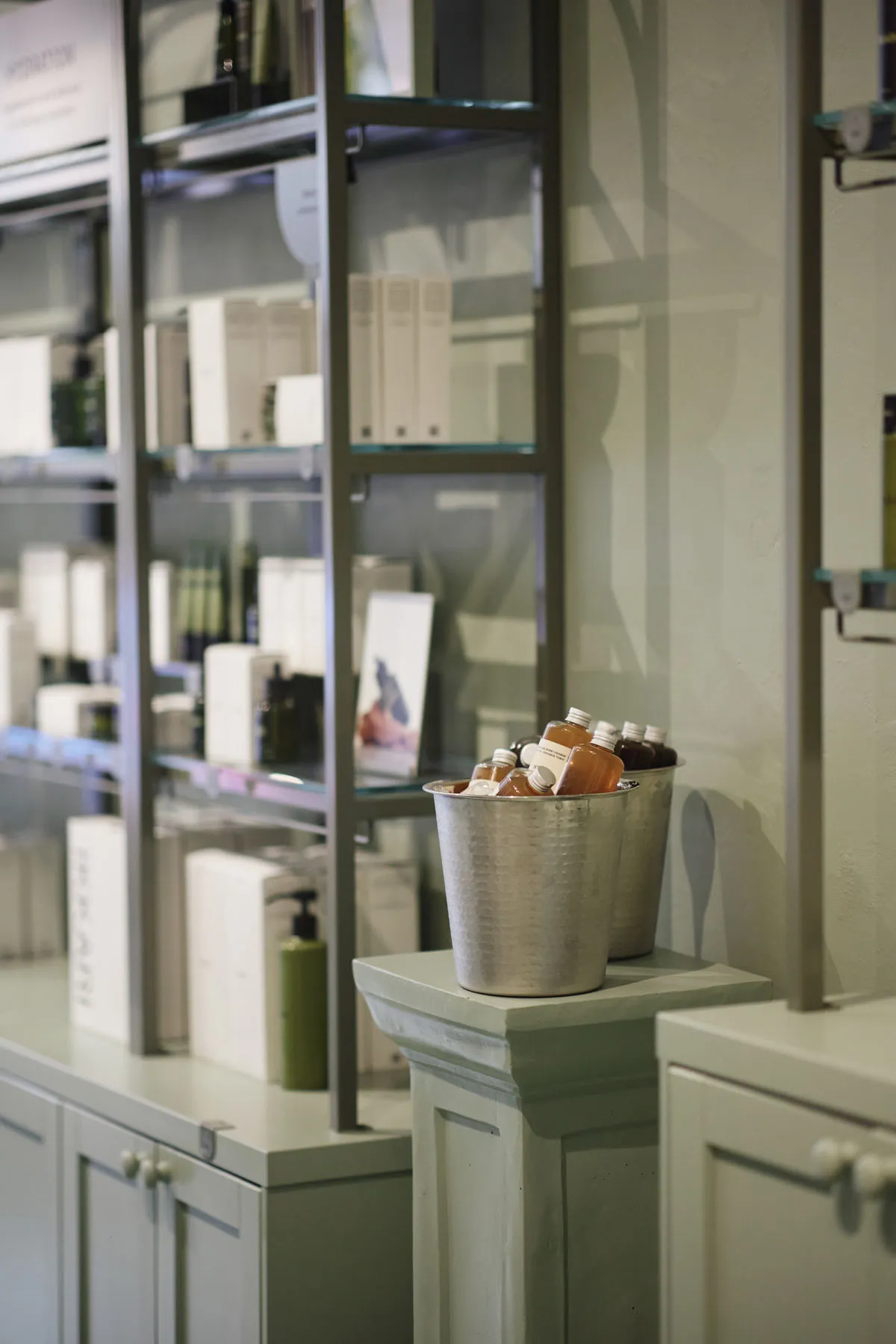 Retail cosmetics store display featuring metal containers with bottles of orange liquid and glass shelving.
