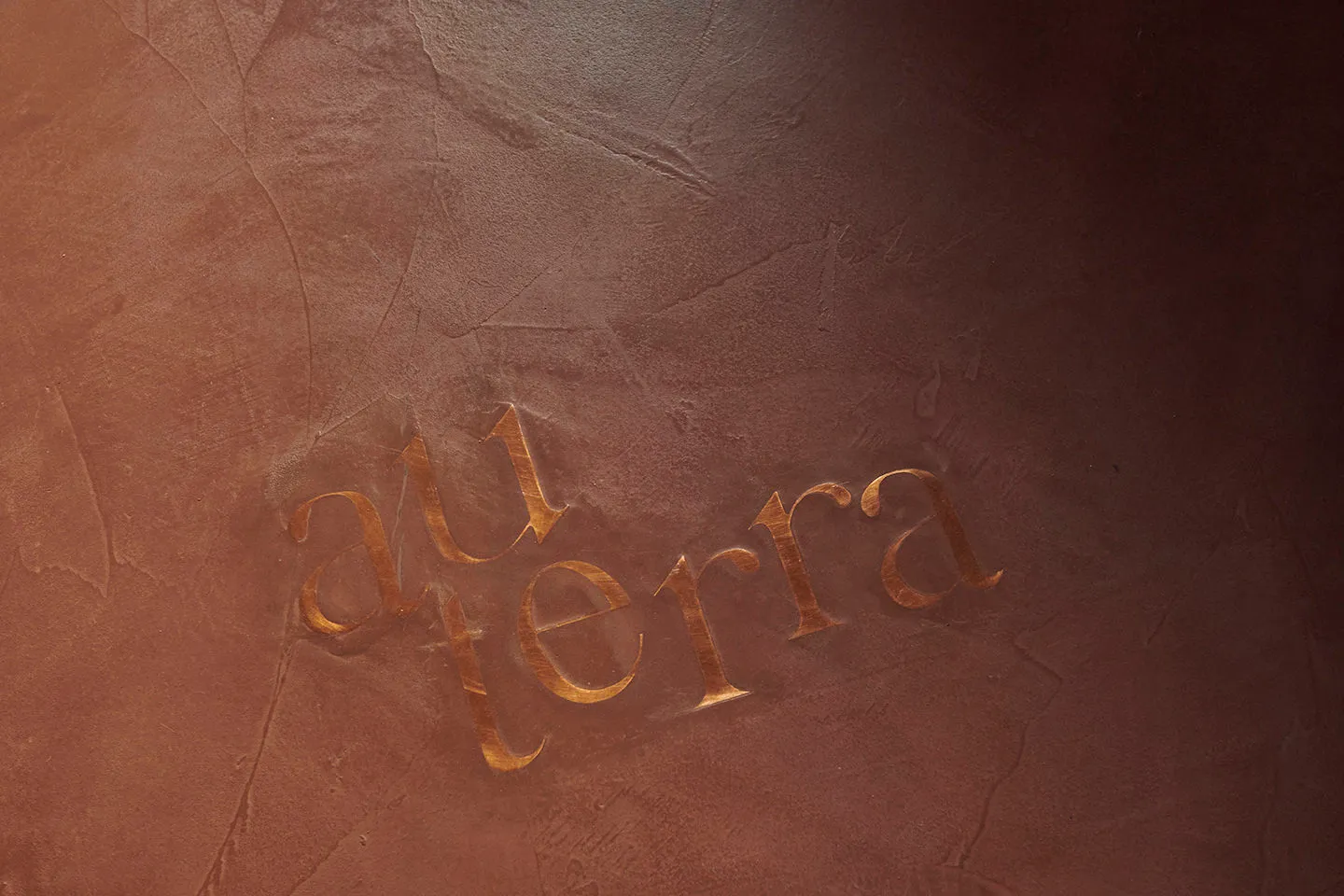 Gold-colored metallic inscription carved into a textured wall, featuring stylized letters spelling 'au terra'.