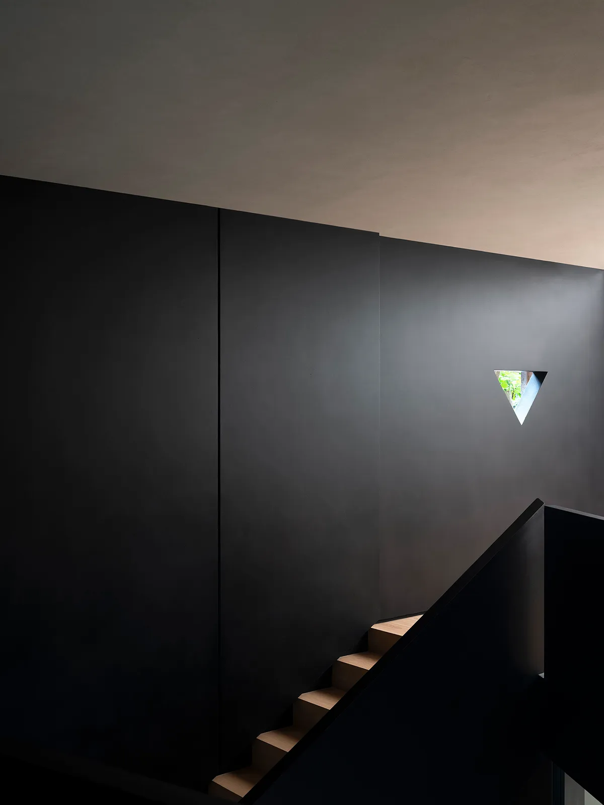 Modern, minimalist interior space with a black staircase, concrete walls, and a triangular window.