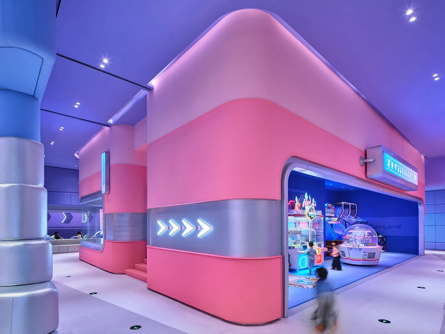 A vibrant game center with pink and blue lighting, featuring a bright, colorful environment with game machines and a playful