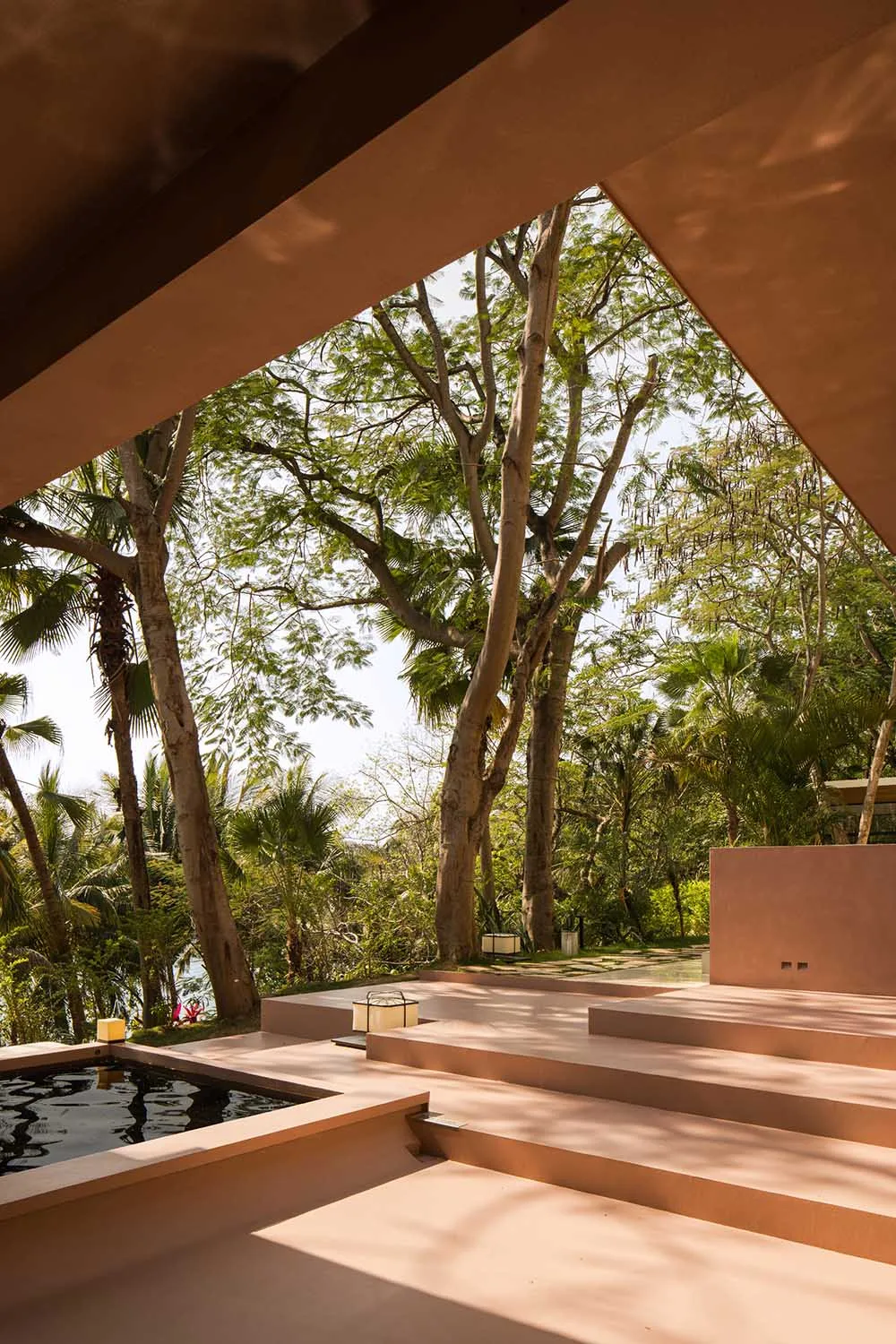 Modern outdoor living space with concrete steps and a pool surrounded by lush greenery.