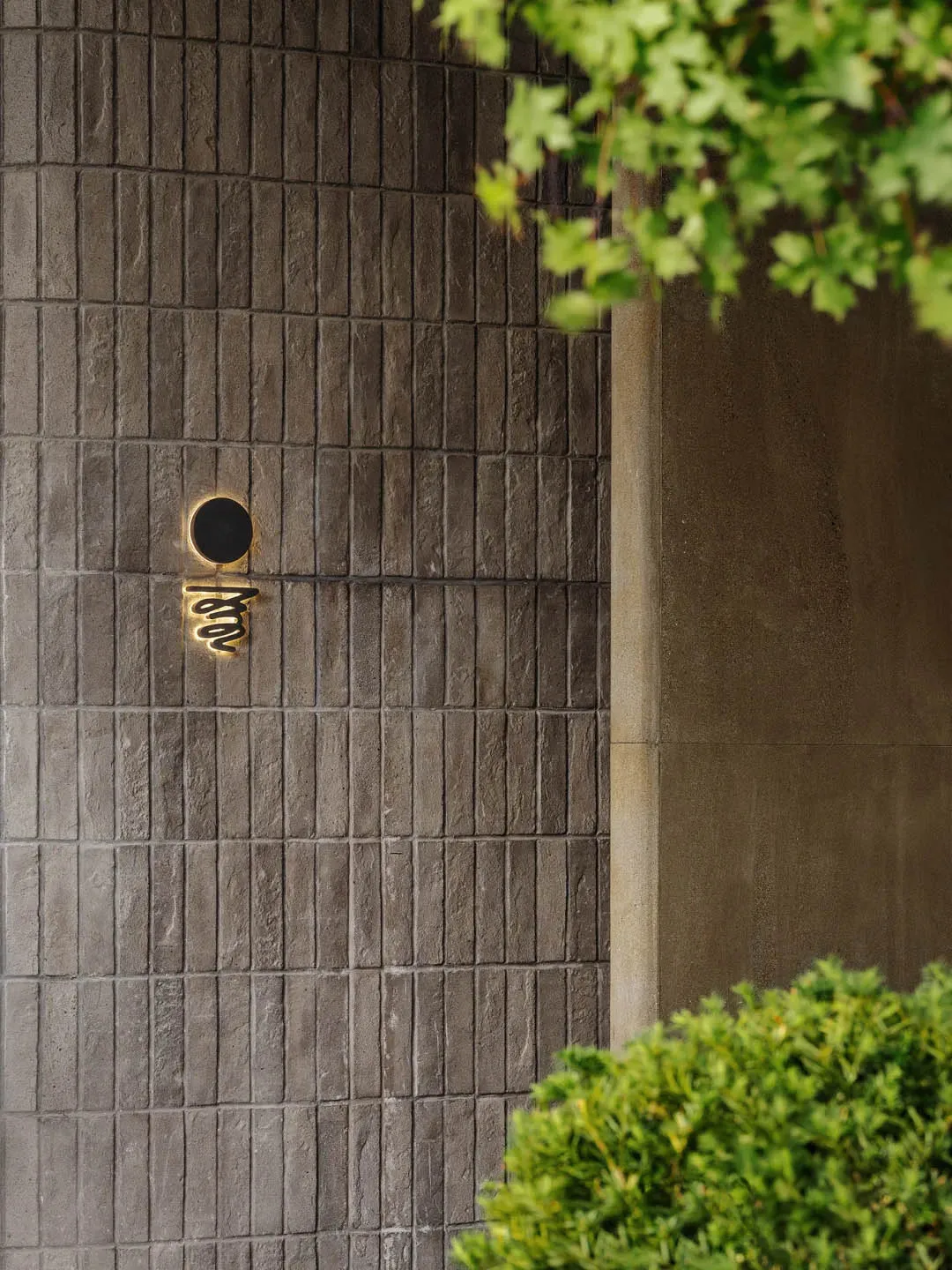 Modern building exterior made of concrete tiles with a circular window and cursive text.