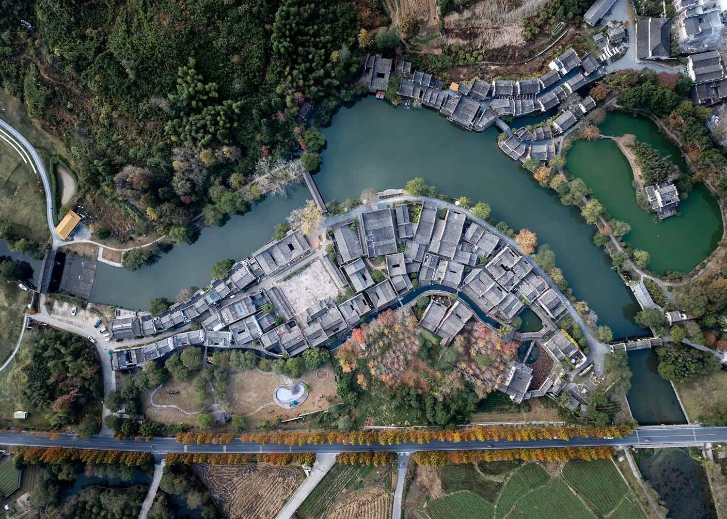 Aerial view of a traditional Chinese village with curved rooftops and a central water feature.