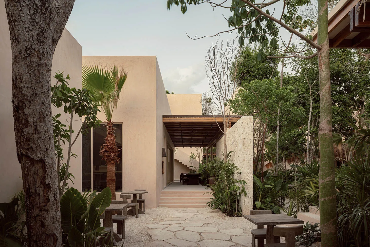 Concrete patio with wooden seating surrounded by lush greenery and palm trees.