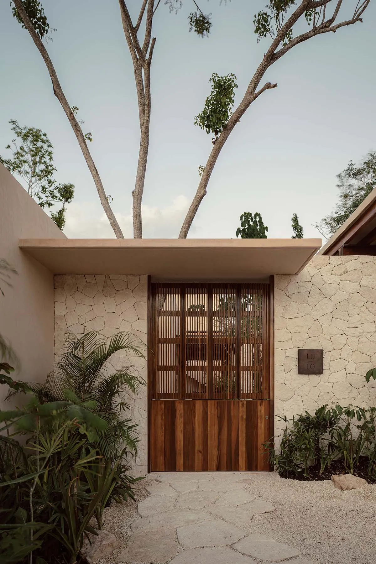 Modern entranceway featuring a wooden double door with a疼痛守卫, surrounded by natural greenery and textured stone pathway.