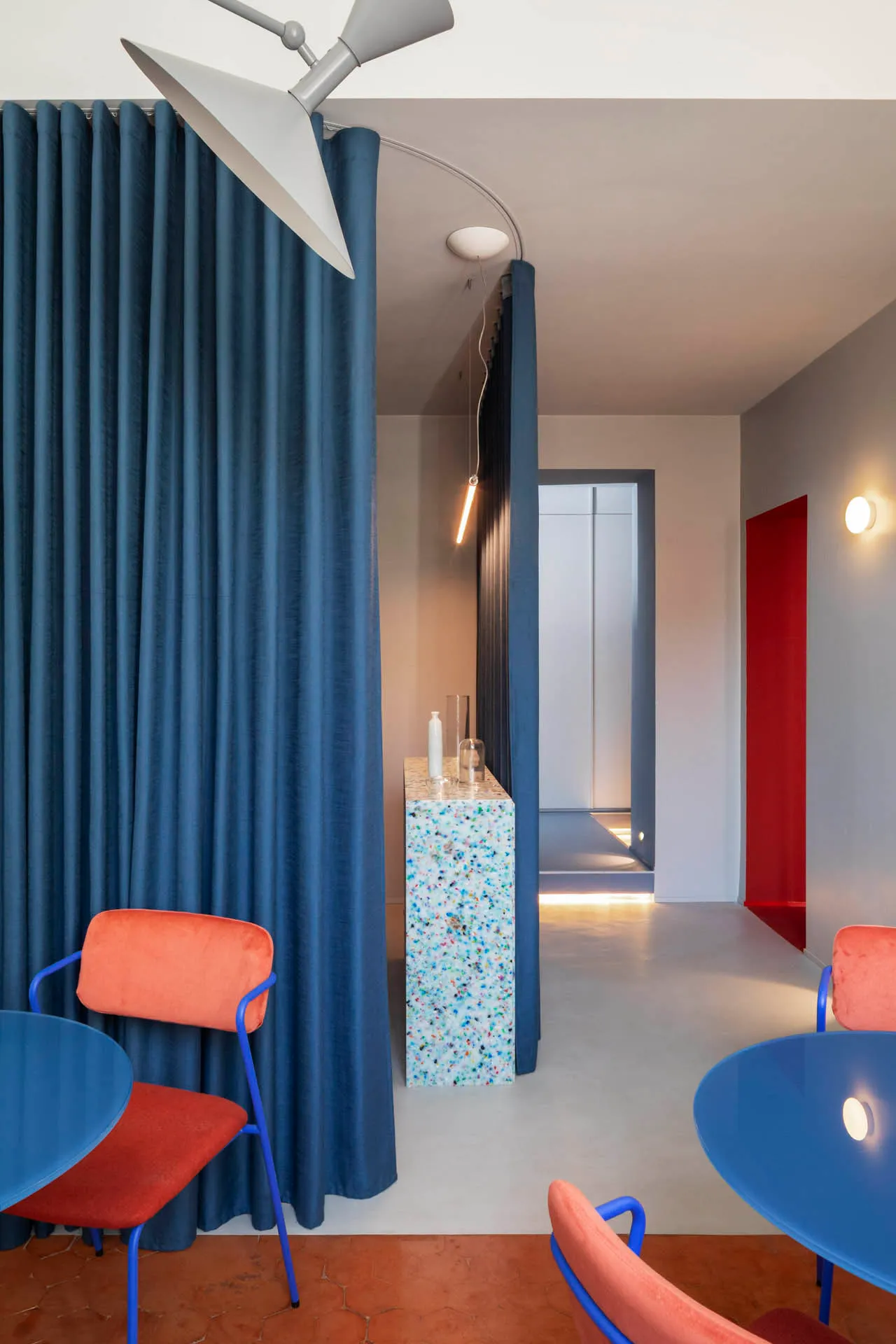 Modern industrial office space with concrete walls, glass partitions, blue tiles, and L-shaped furniture.