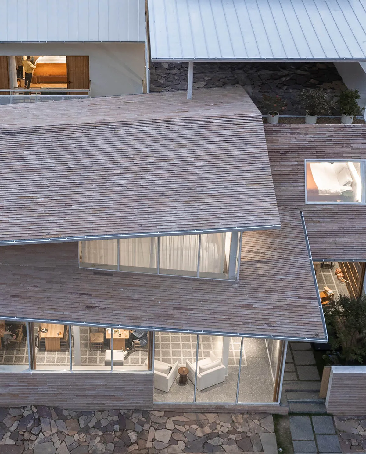 A modern house with wooden exterior and large windows overlooking a courtyard.