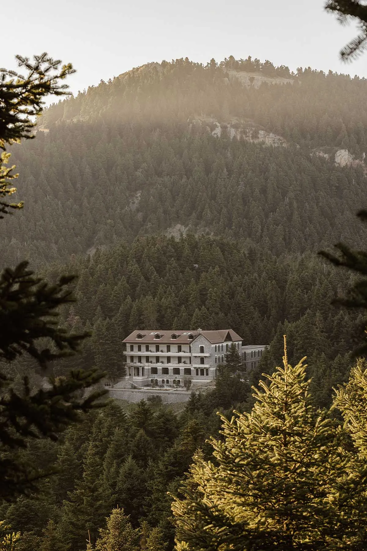 A stone hotel building nestled in a forested mountain landscape.