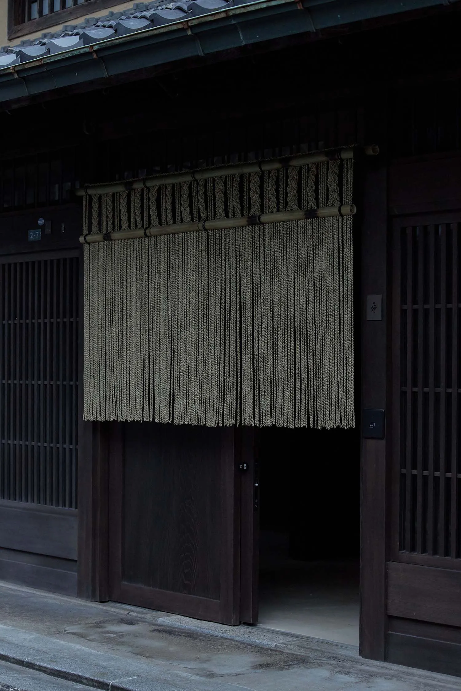 A traditional Japanese storefront with a rope curtain hanging from above.