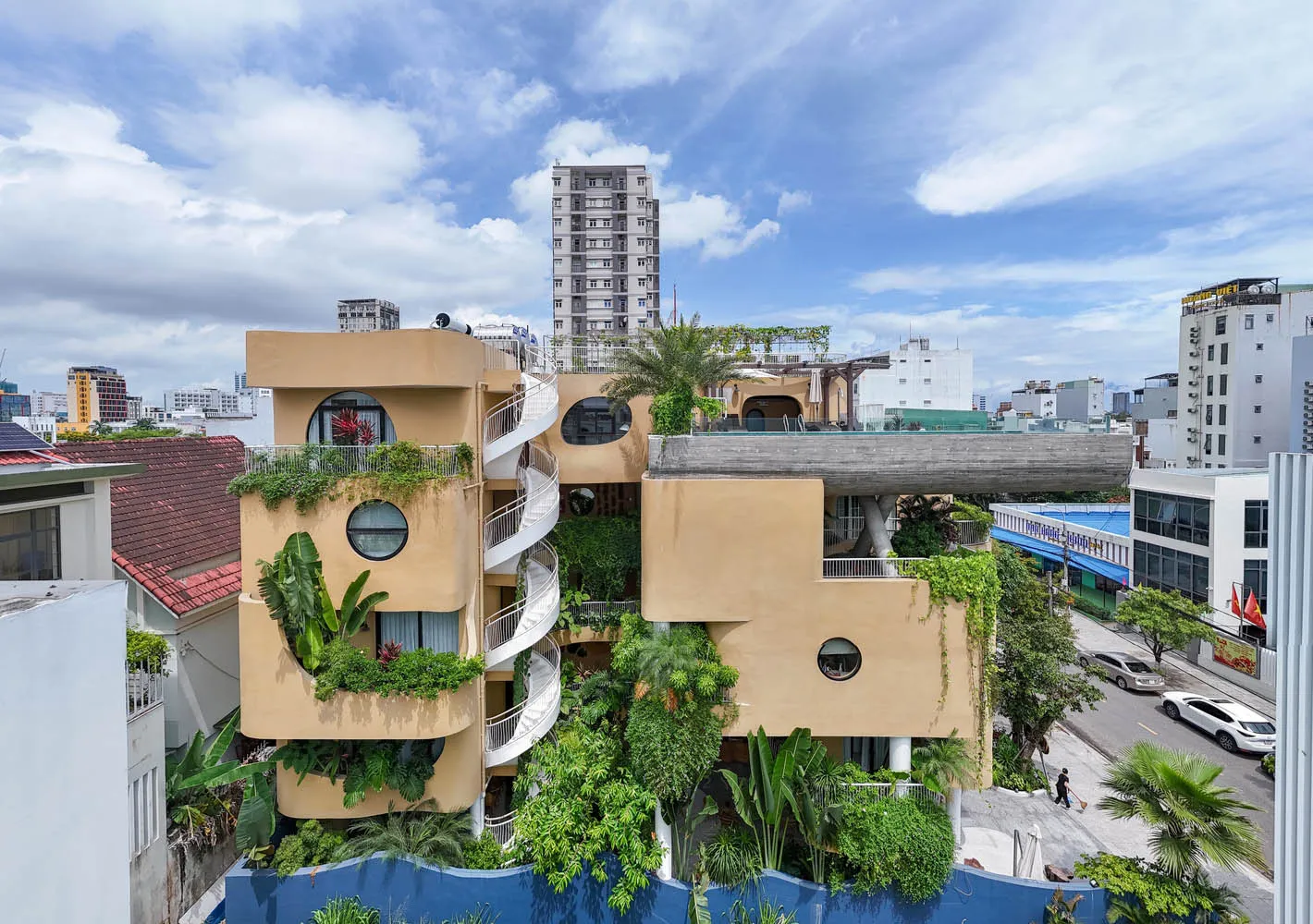 一座現代建築,外觀以混凝土與玻璃為主,搭配綠意植栽與陽台。