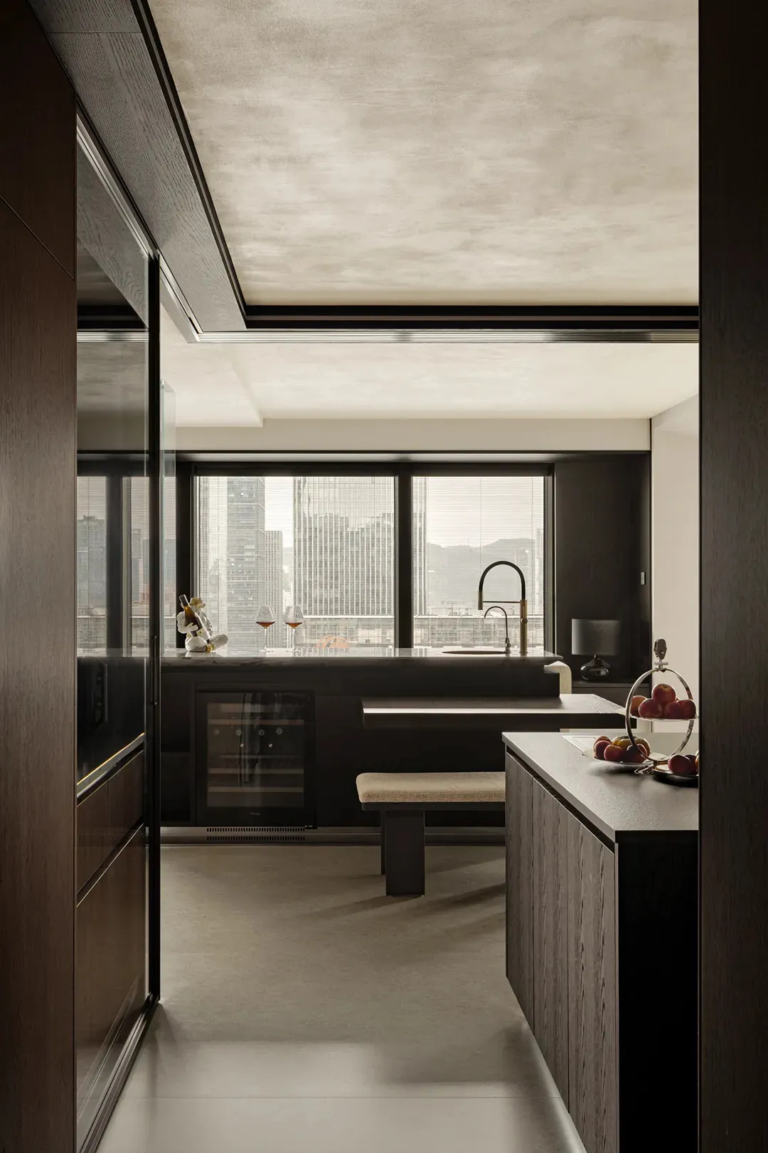 A modern kitchen with dark wooden elements and marble countertops, featuring a large window with a cityscape view.