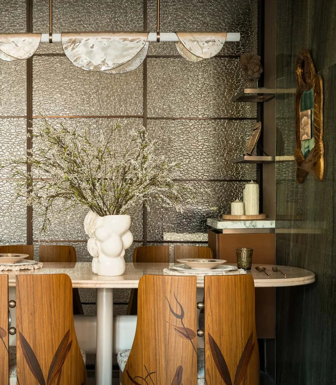 Modern dining room featuring wood chairs, marble table, and metallic pendant lights.