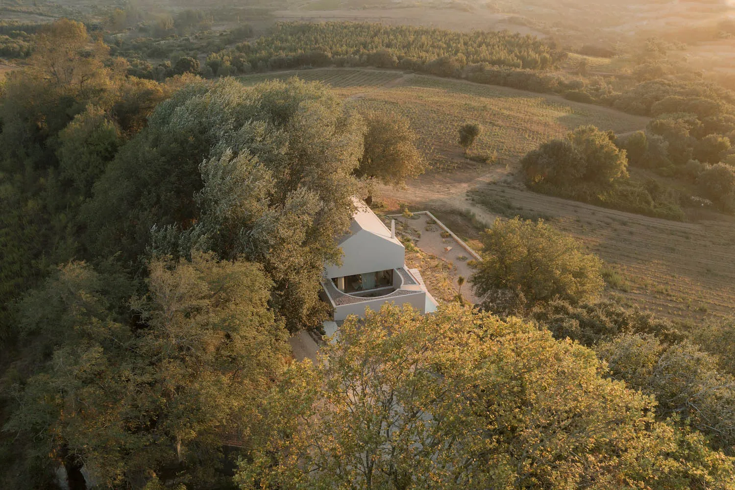 A minimalist house made of white concrete, surrounded by green trees and fields.