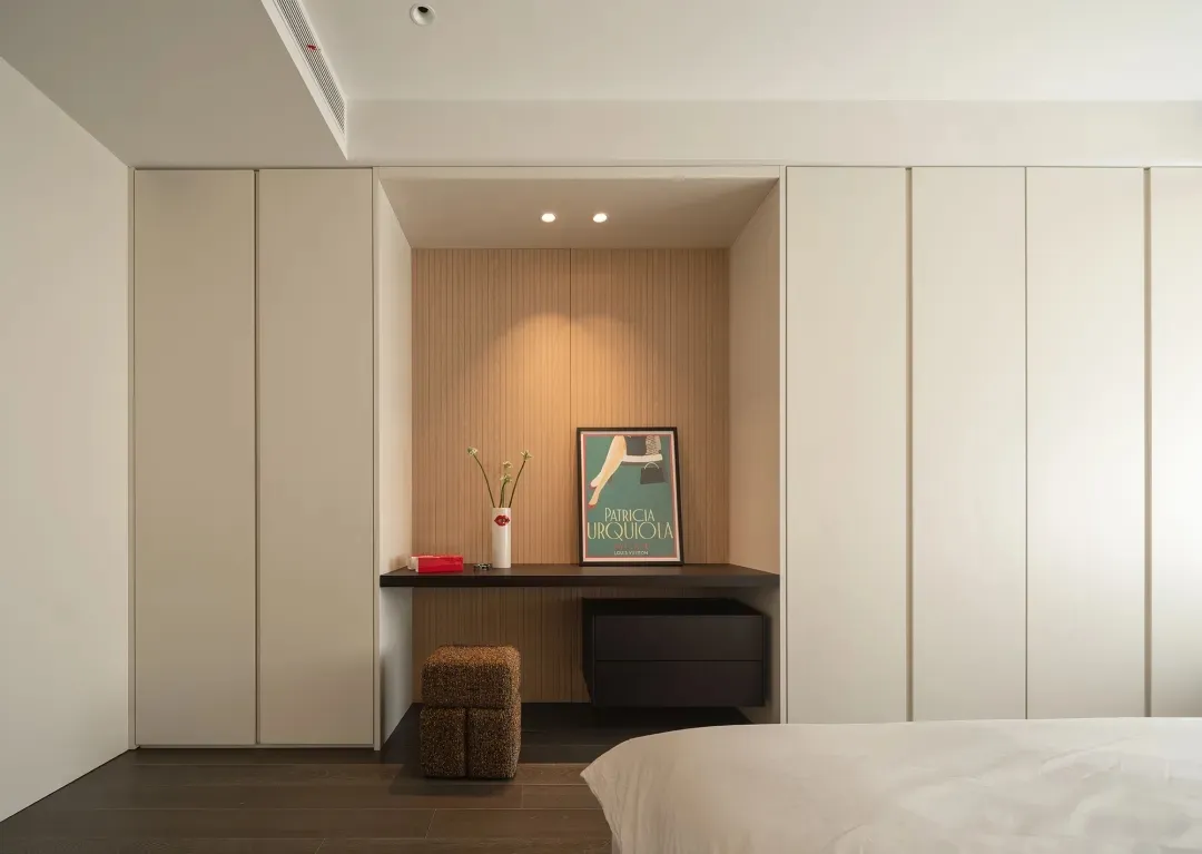 A minimalist bedroom with a bed, white bedding, a wooden desk, and a poster on the wall.