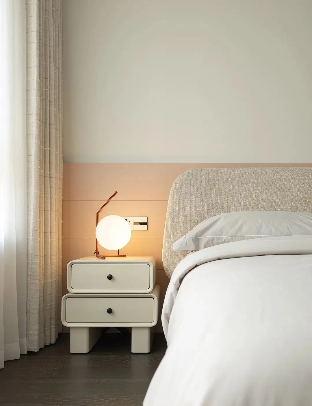 Minimalist modern bedroom with fabric bed, white bedding, and white nightstand with a round lamp.