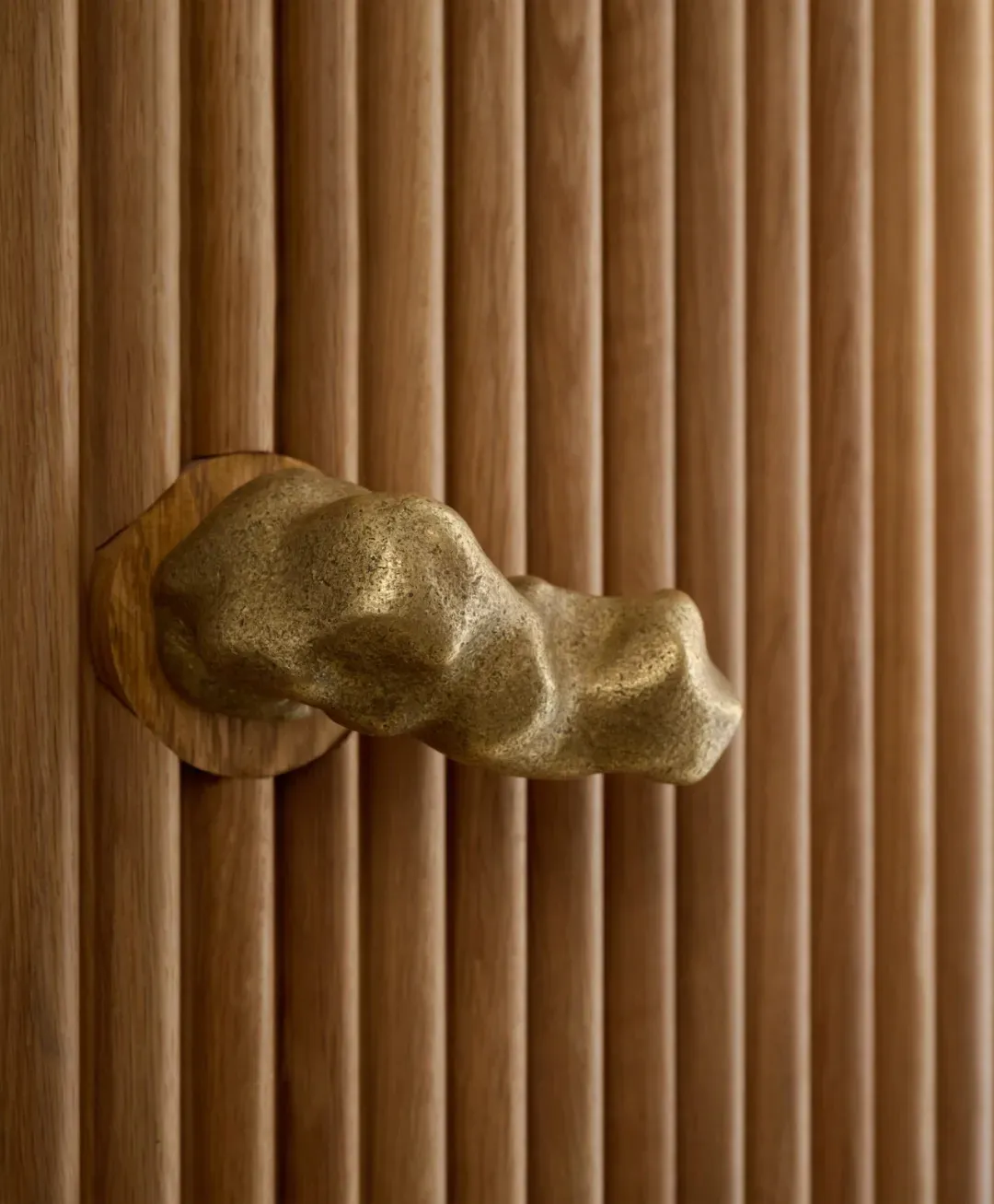 A sculptural brass door handle mounted on a wooden paneled door.