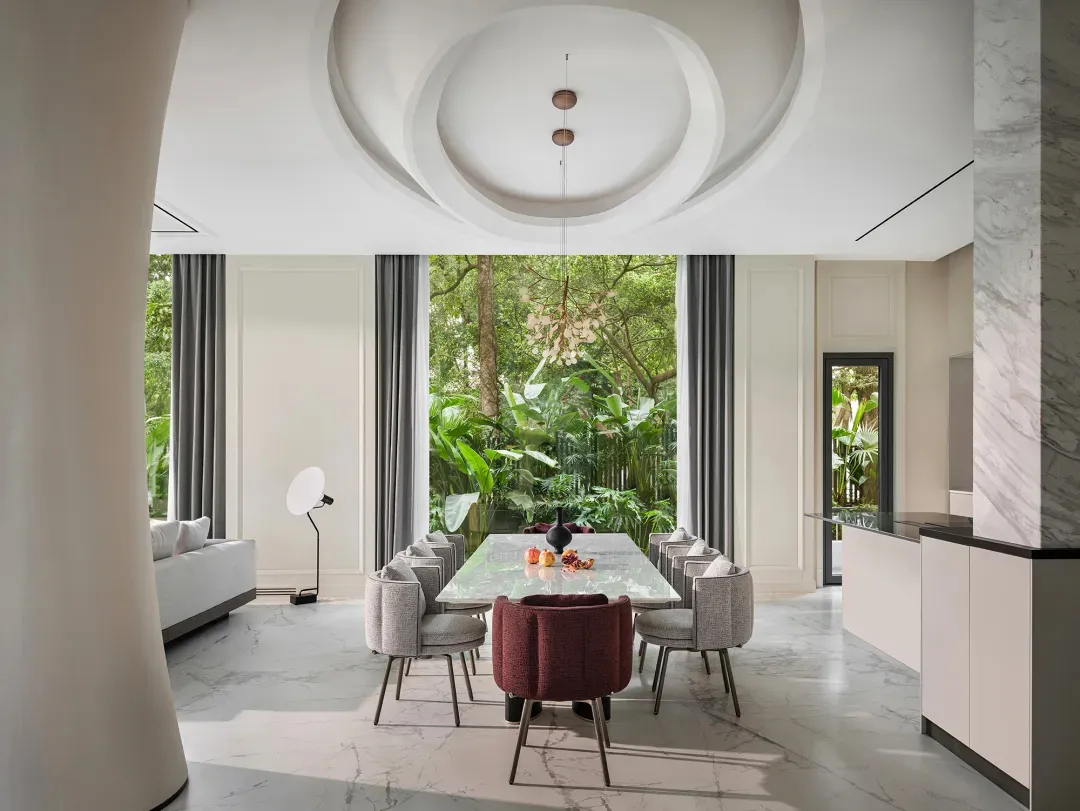Modern dining room with a marble table surrounded by fabric chairs, featuring a large garden view.