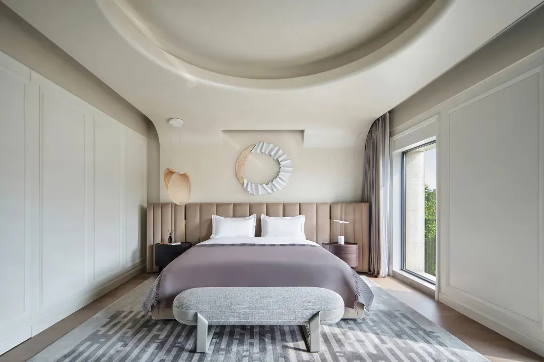 Modern minimalist bedroom with a cozy bed, decorative mirror, and large window.