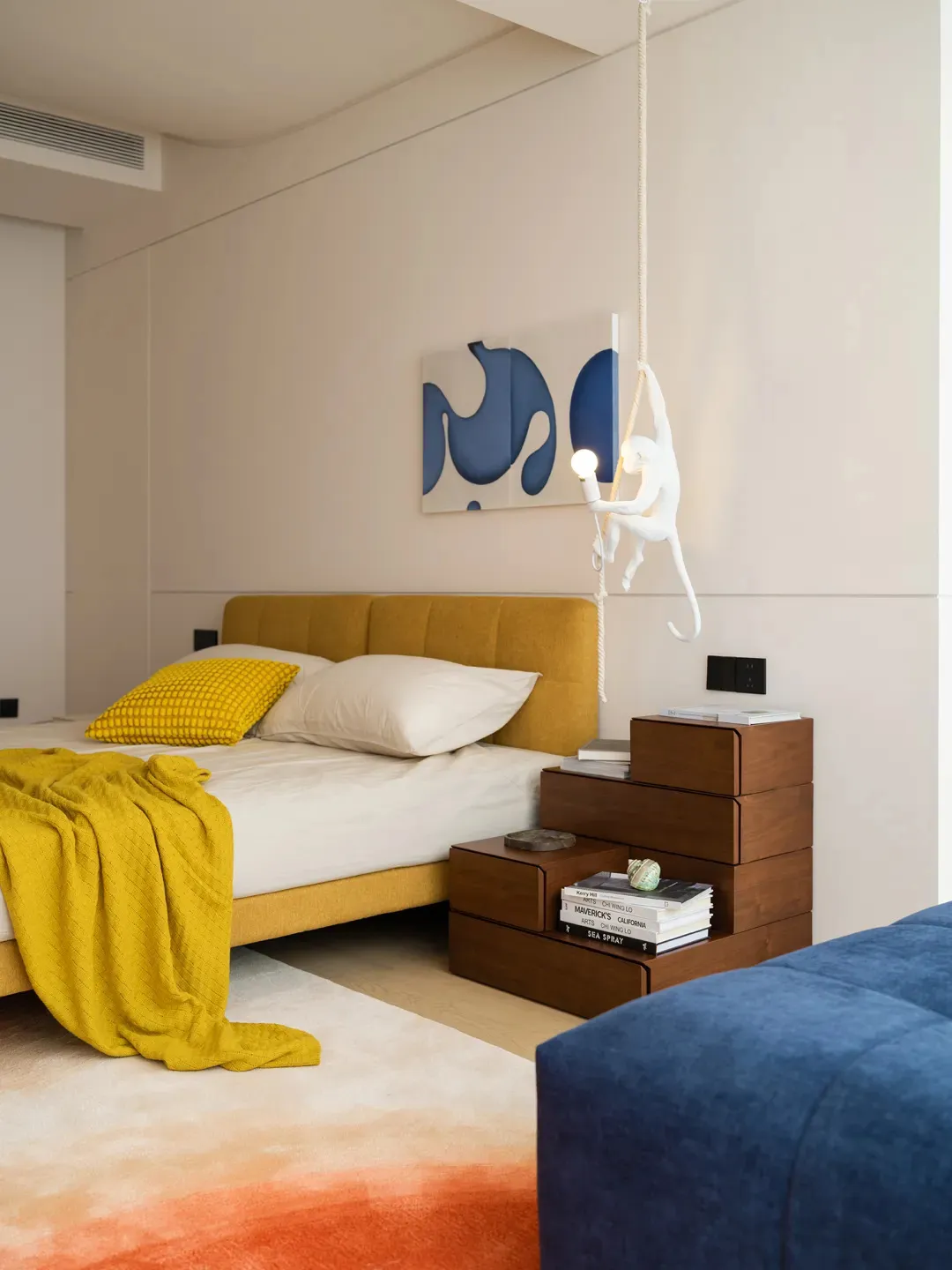 Modern minimalist bedroom featuring a yellow upholstered bed, wooden nightstands, and a creative hanging monkey light fixture