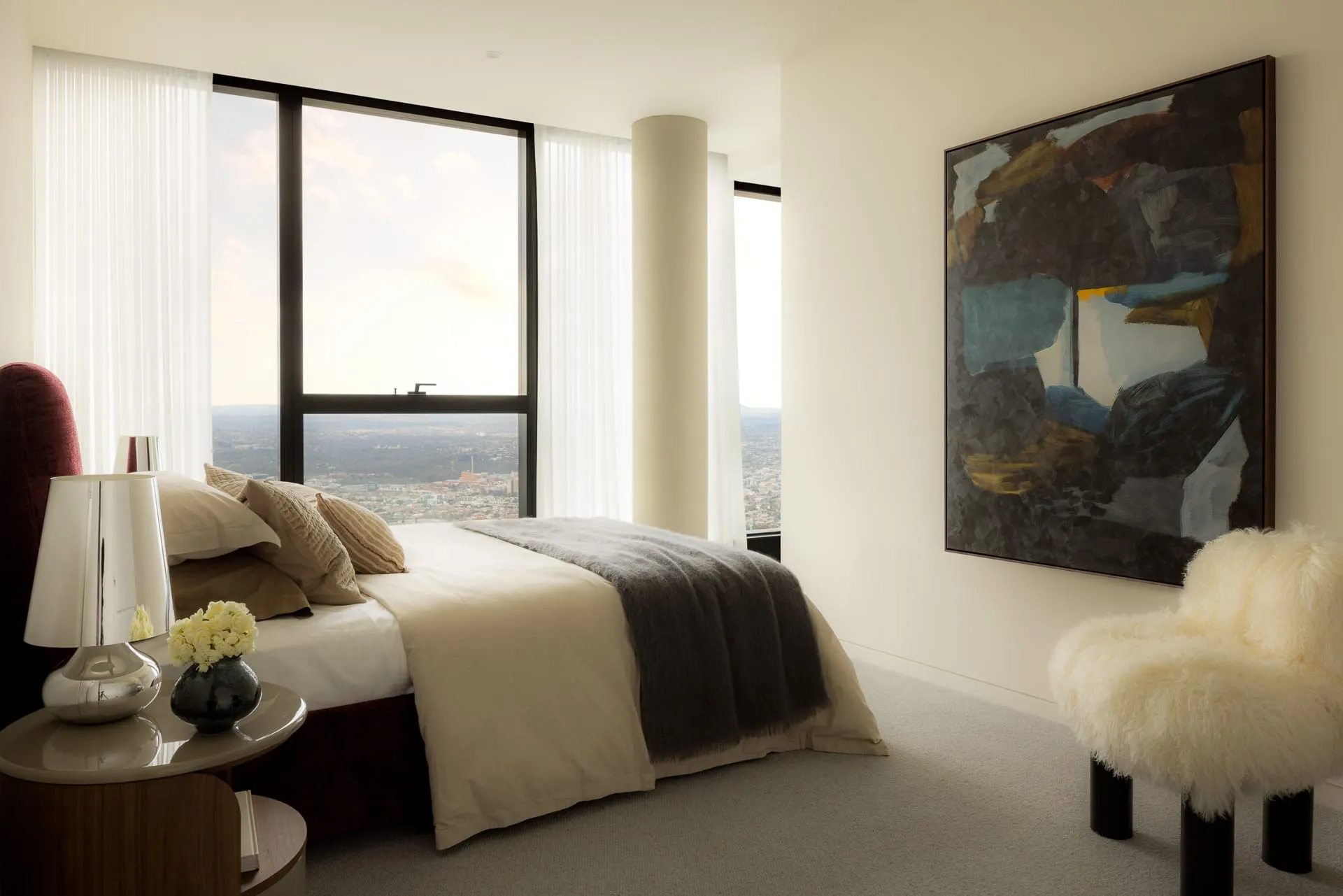 Modern bedroom with a large bed, abstract art, and a view of the city through sheer curtains on the window.