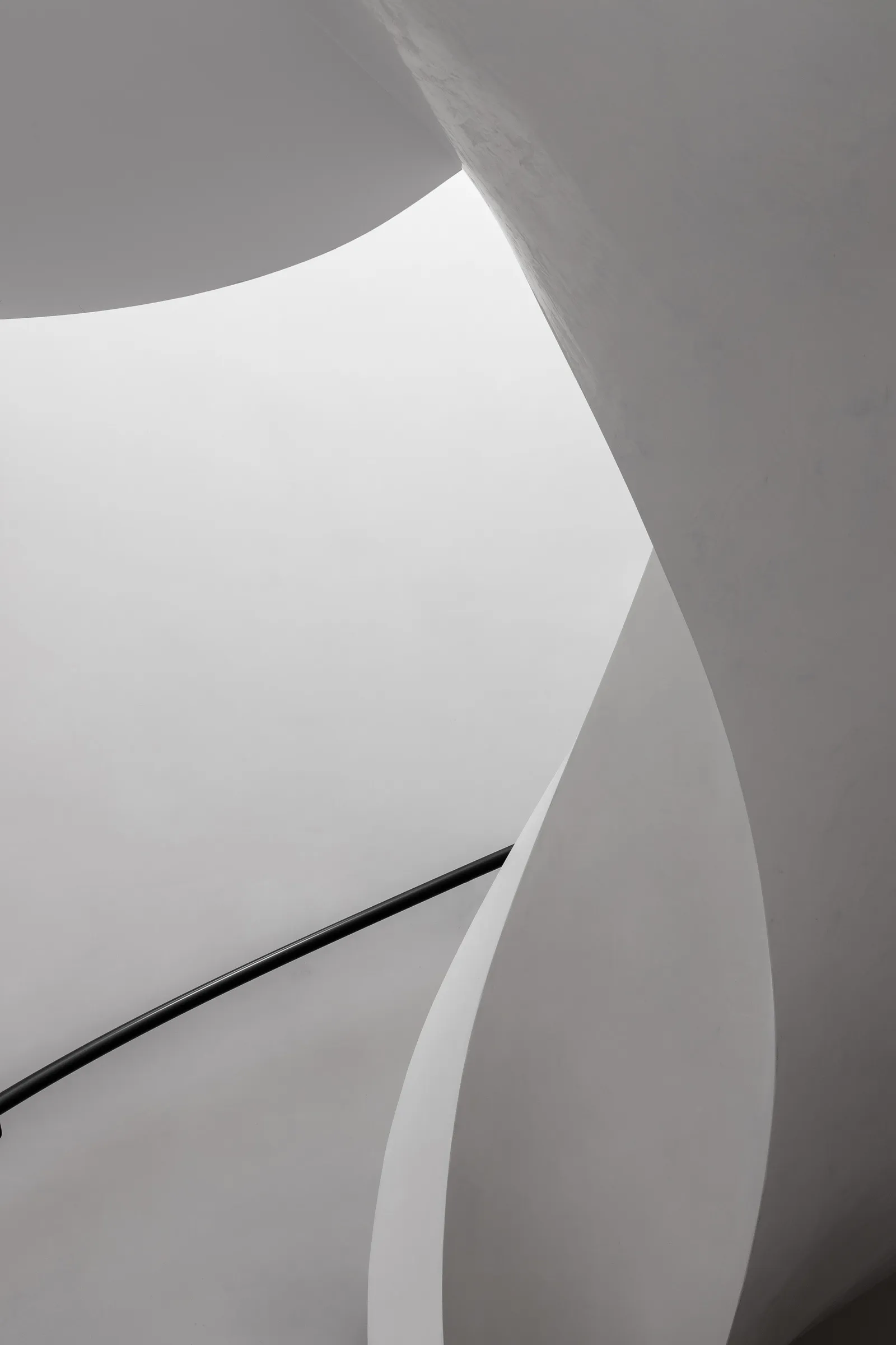 Curved white concrete stairs with a black handrail in a modern interior space.