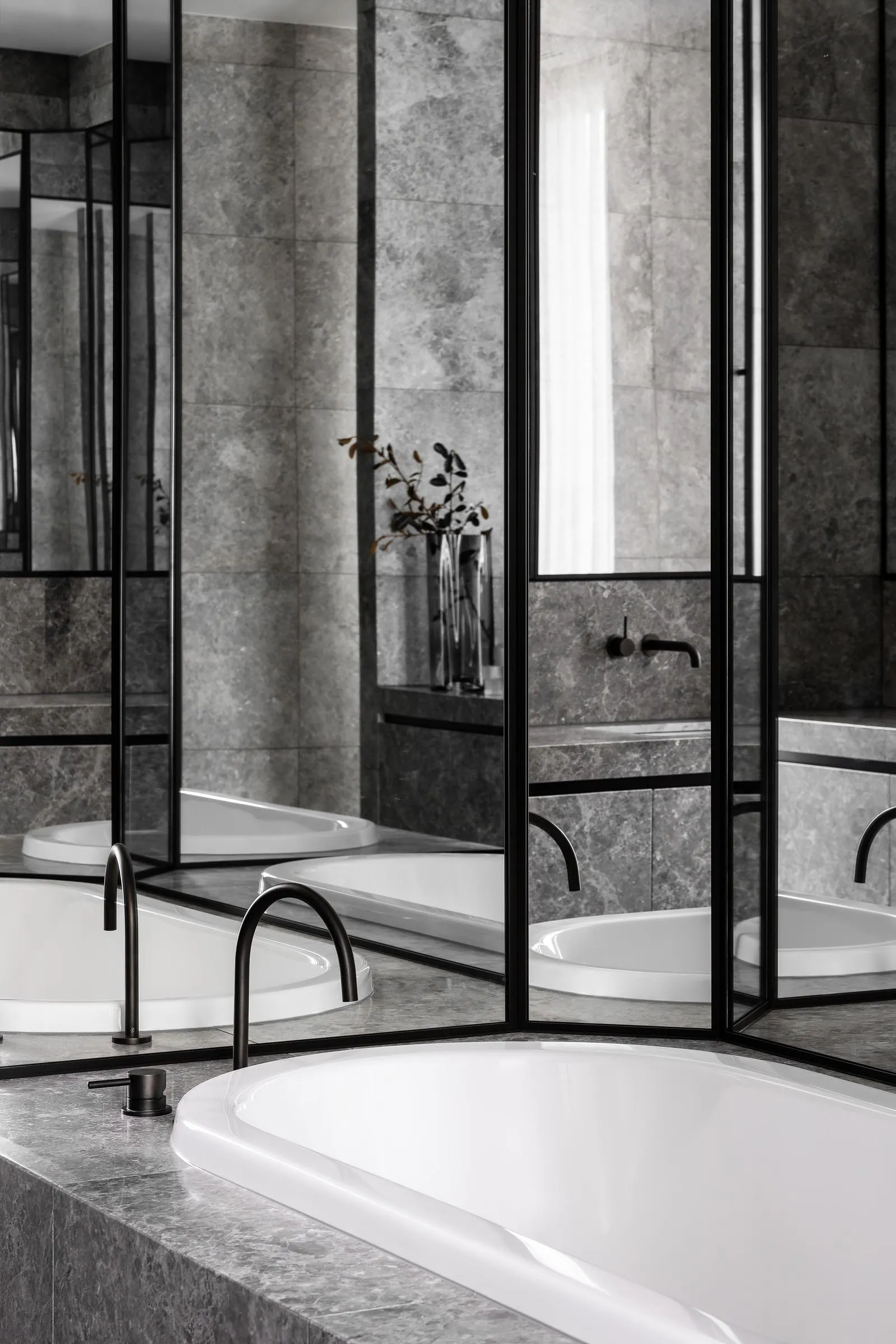 Modern, minimalist bathroom featuring grey marble tiles and a sleek white bathtub.