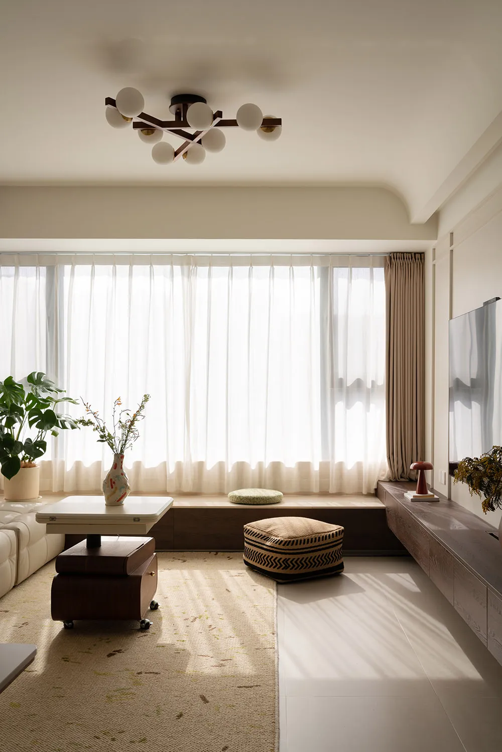 Modern minimalist living room with wood furniture, glass windows, and metal light fixture.