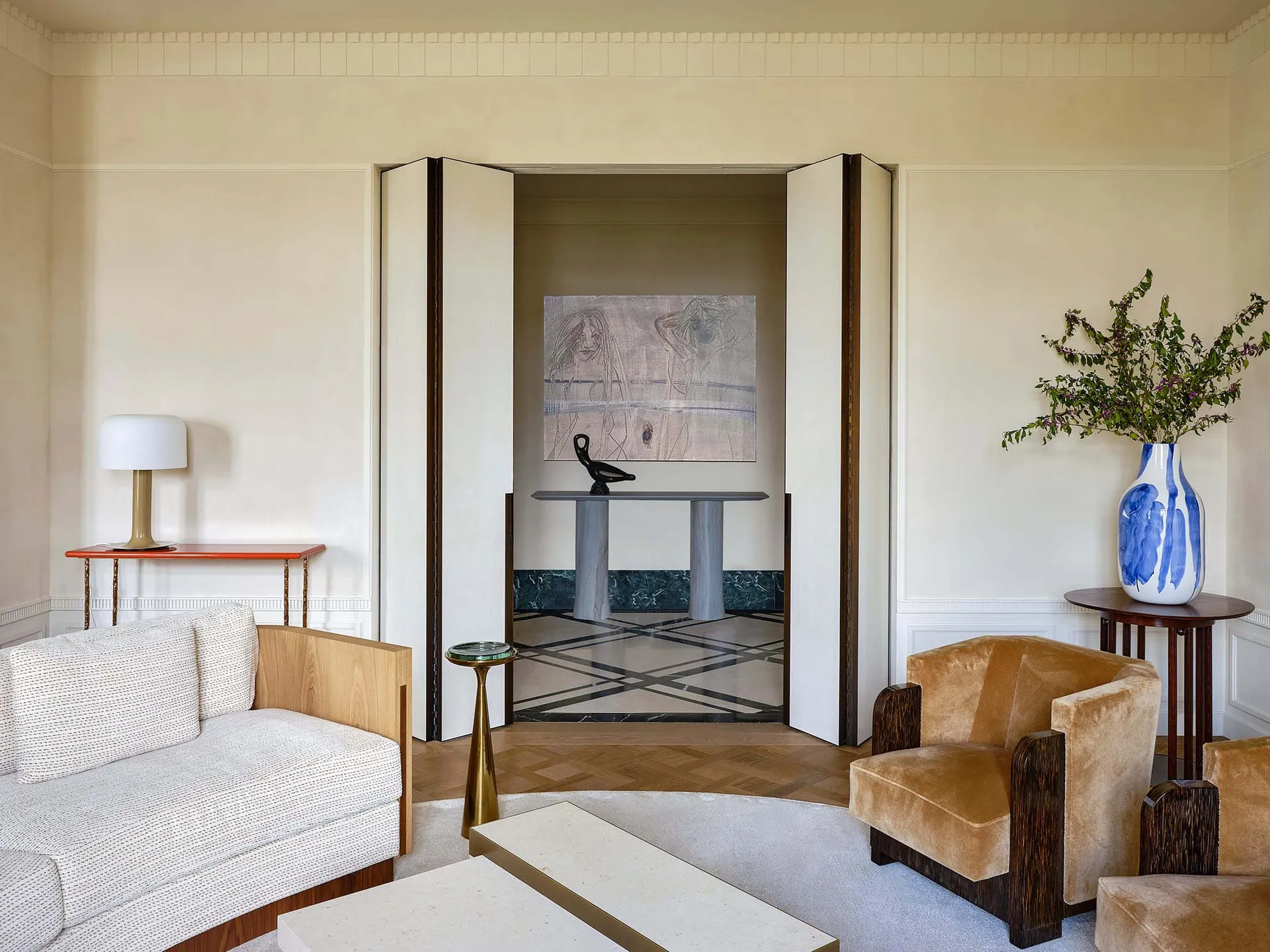 Modern living room featuring white walls, wooden floor, and a white sofa with a side table and lamp, leading to a hallway wit