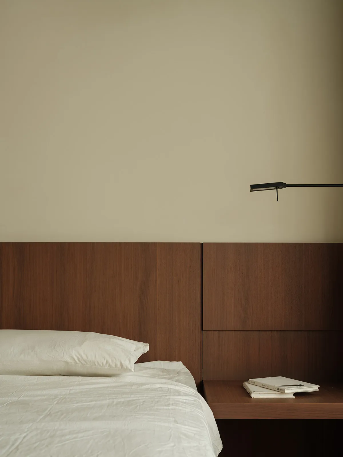 Modern, minimalist bedroom featuring wooden headboard and floating nightstand with books.