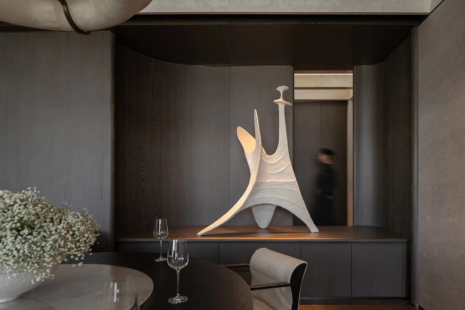 Modern minimalist dining room with concrete walls, wooden table, and abstract sculpture.