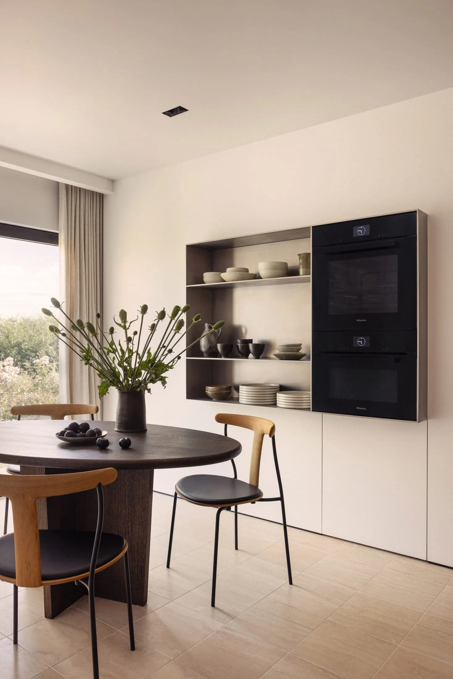 Modern kitchen featuring wooden table and chairs with stainless steel appliances and open shelving.
