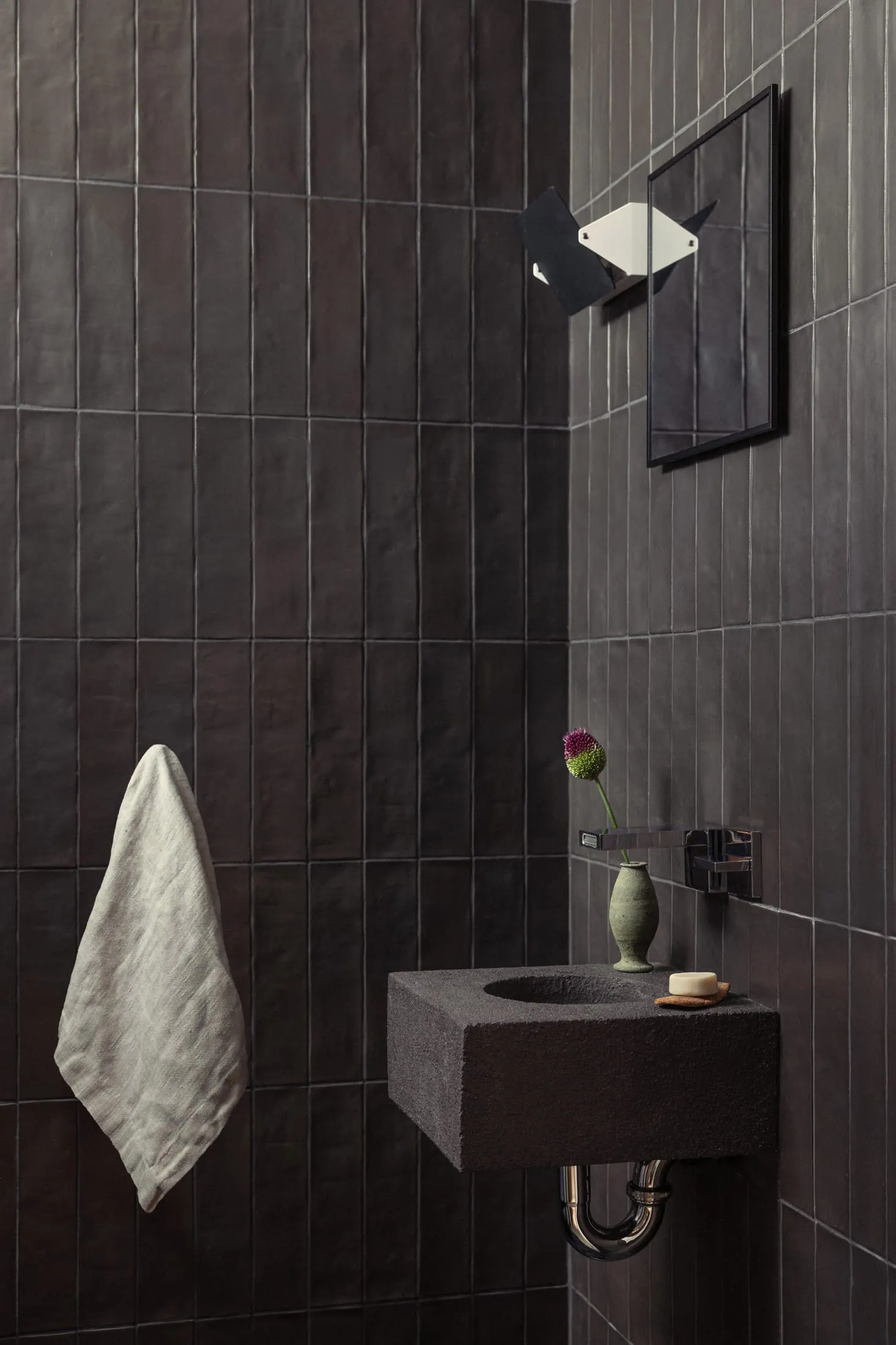 Concrete corner sink with a vase of flowers and a bar of soap in a minimalist bathroom setting.