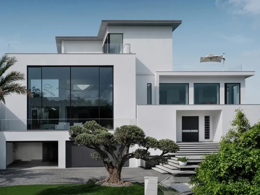 Modern house exterior with large glass windows, white walls, and a minimalist design.