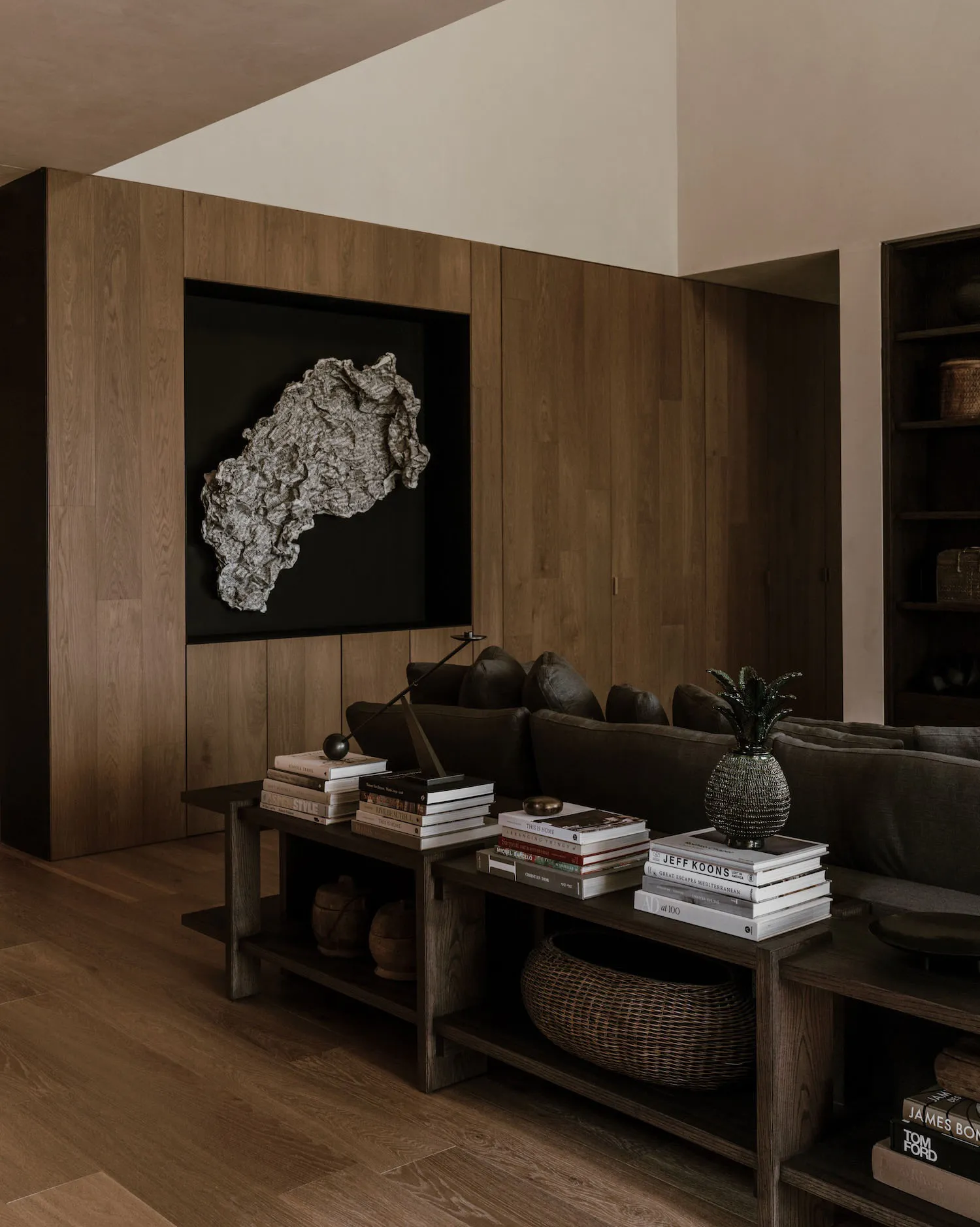 A modern interior design featuring a wooden living room with a plush sofa, books, and a unique sculpture on a black backgroun