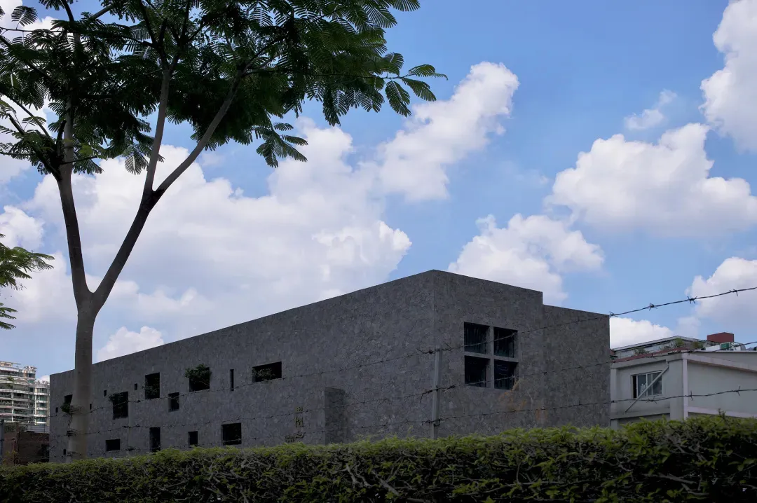 A modern building with a concrete facade and large windows against a blue sky with white clouds.