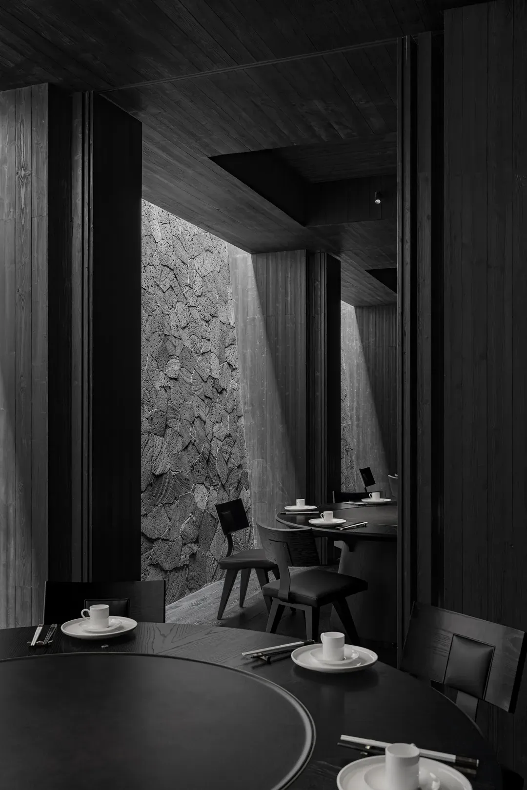 A modern minimalist restaurant interior with dark wooden and concrete materials.
