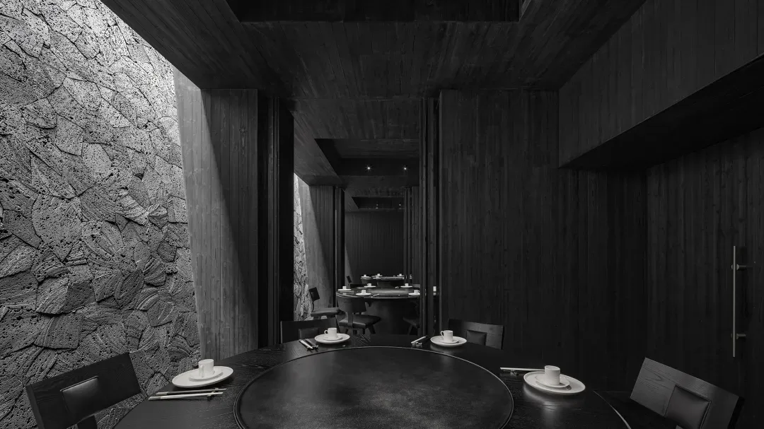 A modern restaurant interior with black tableware, chairs, and a stone wall, featuring a round table and minimalist decor.