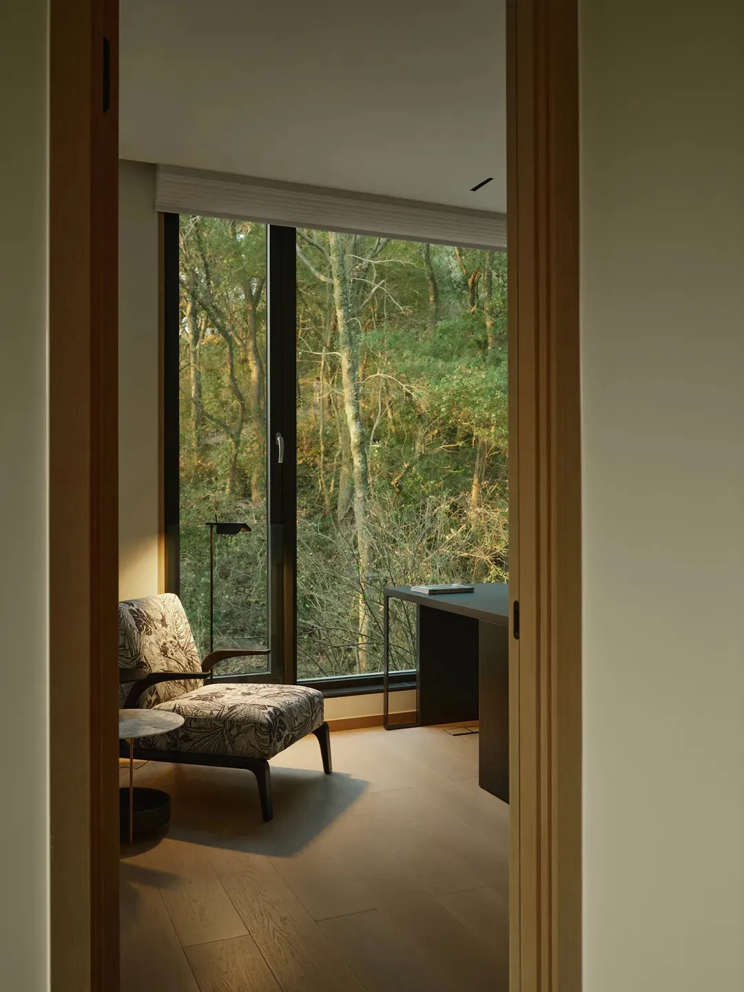 Modern residential interior featuring a cozy seating area with a floral-patterned armchair and a wooden floor, with a view of