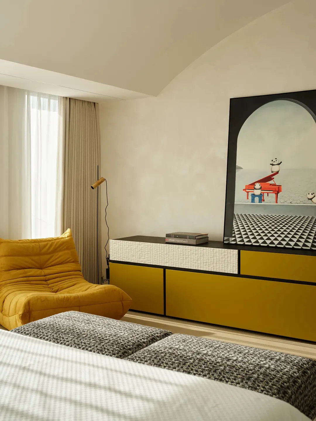 Modern minimalist bedroom featuring a yellow upholstered chair, a bed with a textured gray and white comforter, and a sideboa