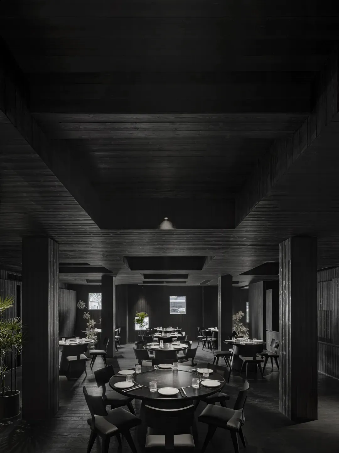 Circular tables and chairs in a minimalist restaurant interior with dark wooden flooring and ceiling.