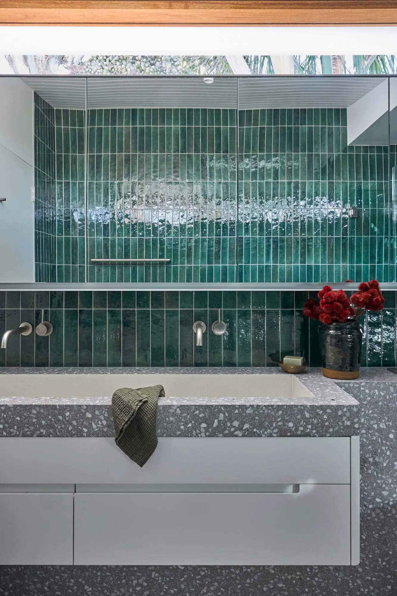 A modern bathroom with green vertical tiles and a concrete countertop, featuring a large bathtub and white cabinets.